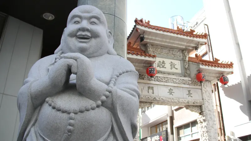 A stone statue of Hotei smiling in front of Changan Gate in Kobe Chinatown